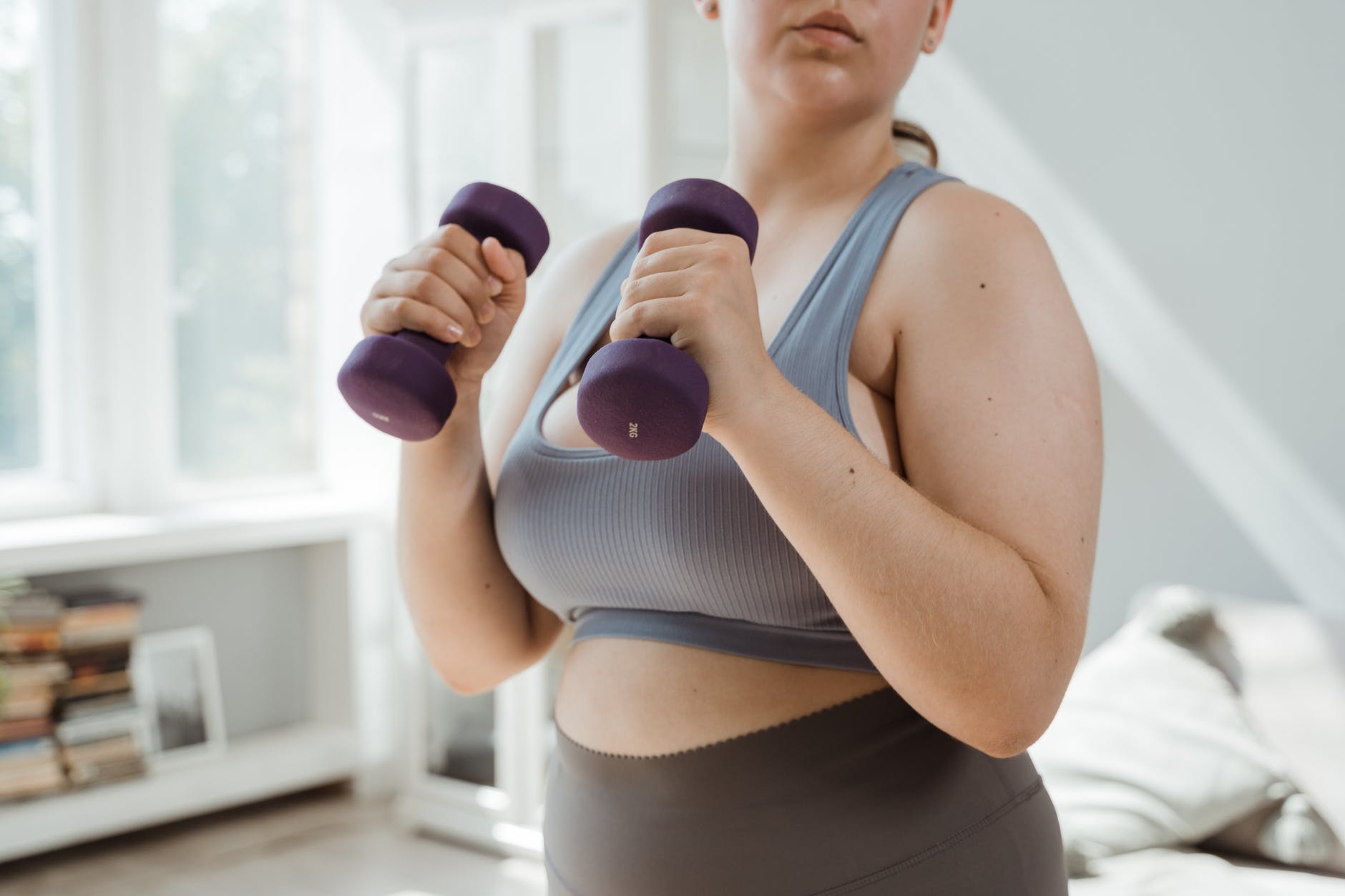 woman in gray sports bra holding purple dumbbells