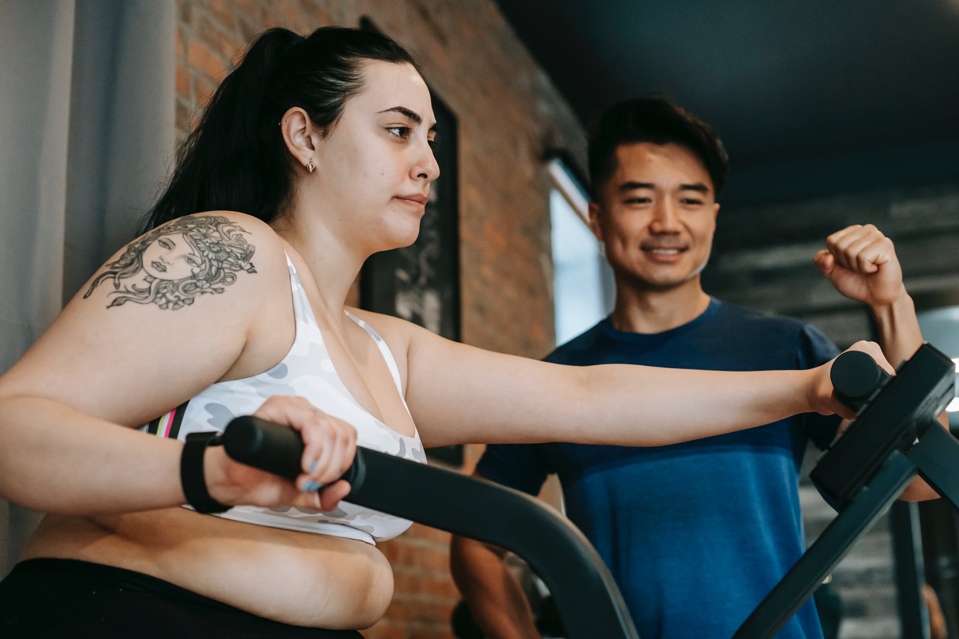 serious young overweight woman doing cardio exercise on elliptical machine with ethnic instructor