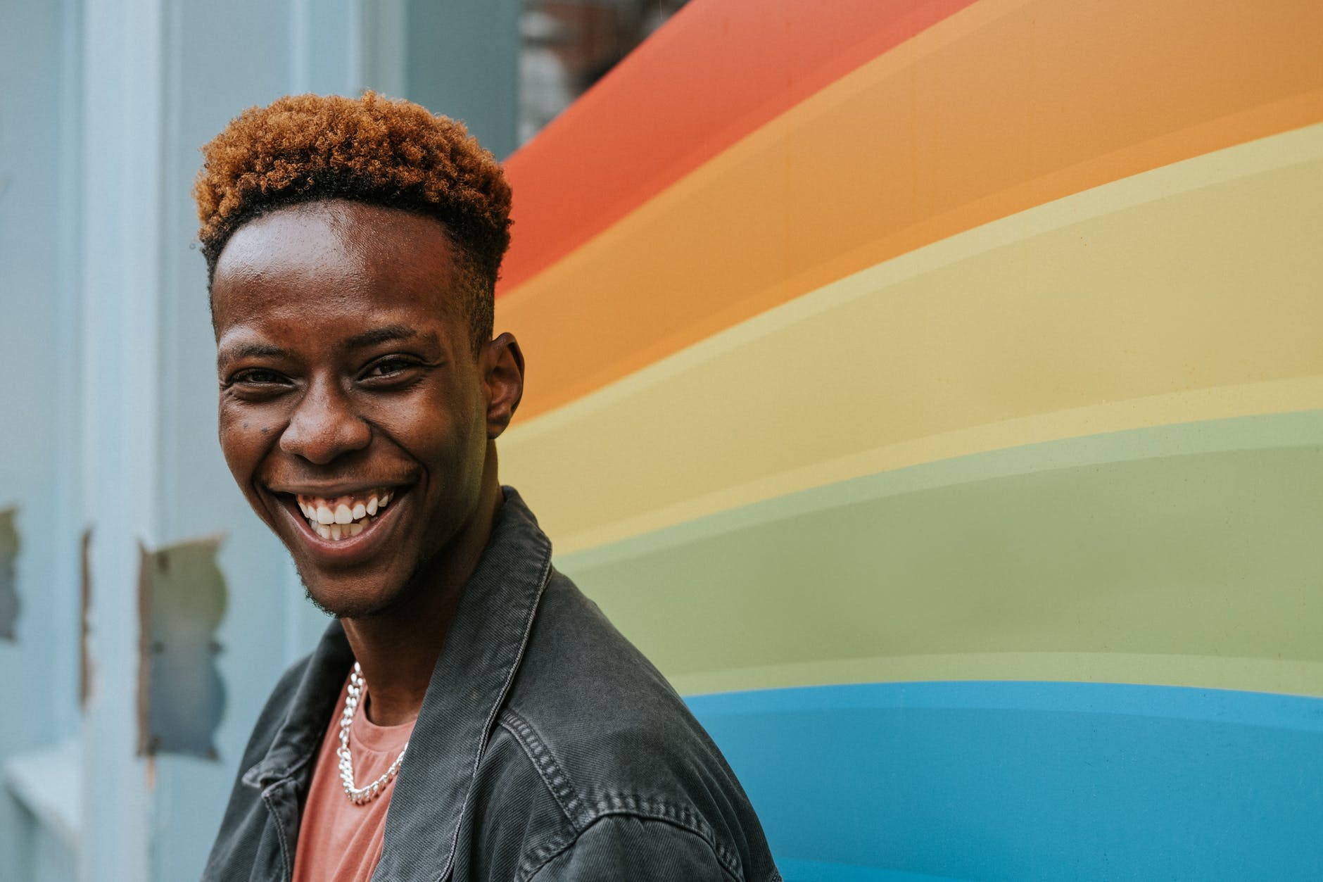 positive young black guy laughing near graffiti wall with rainbow flag