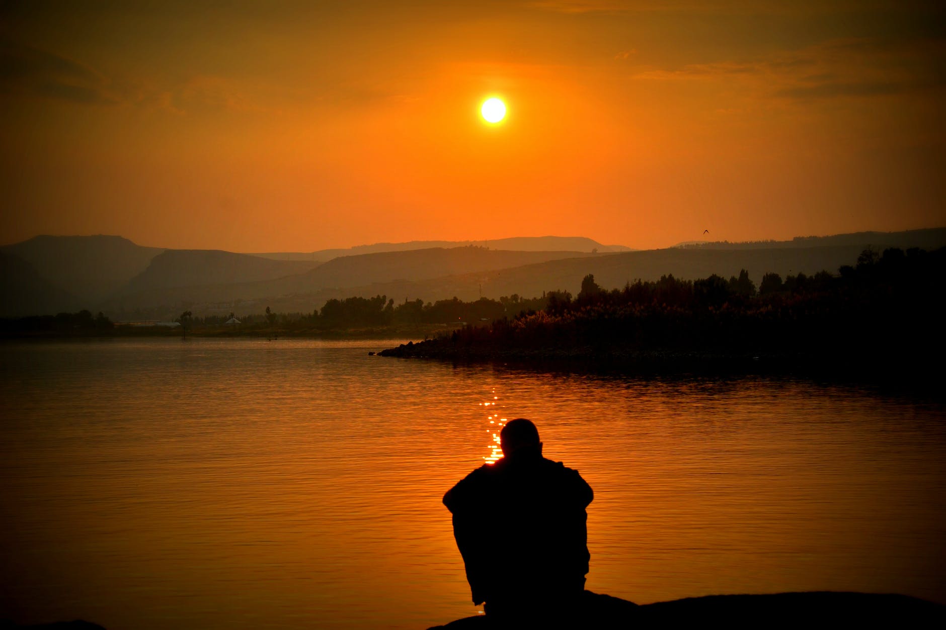 silhouette of person sitting beside body of water thinking negative thoughts